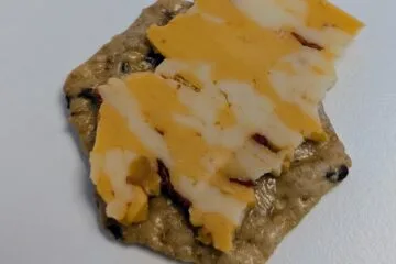 A close-up of a snack featuring Tillamook Spicy Colby Jack cheese on a Crunchmaster cracker