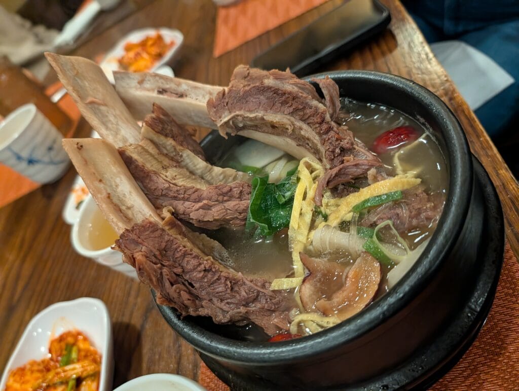 A steaming stone bowl of Galbitang (Korean beef short rib soup) at DuBu, featuring two large bone-in ribs, egg garnish, and a dried jujube date.