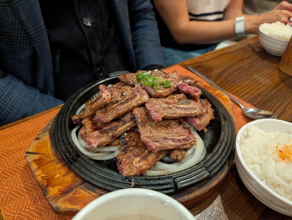 A generous platter of grilled LA-style Galbi (Korean BBQ short ribs) served on a sizzling cast iron plate over a bed of onions at DuBu.
