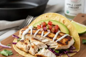 Flaked anti-inflammatory fish tacos with purple cabbage probiotic slaw, creamy Greek yogurt sauce, avocado, and fresh lime on a wooden board.