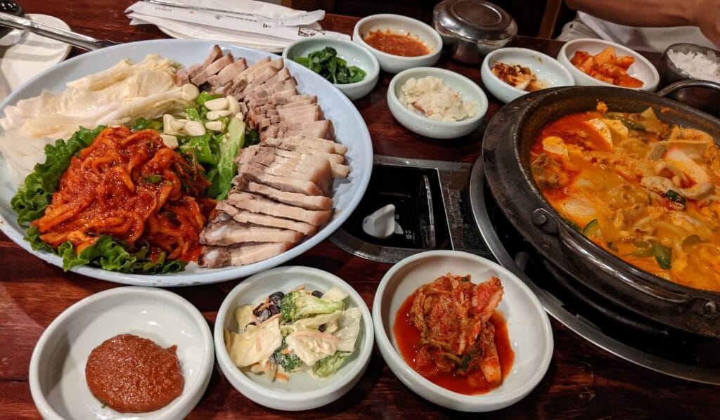 Full table spread at Yechon Korean Restaurant with Bossam (sliced pork belly), spicy kimchi jjigae stew, fresh kimchi, and assorted banchan side dishes.
