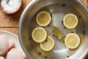 Juicy roasted chicken thigh sliced on cutting board with bowl of wet brine in background