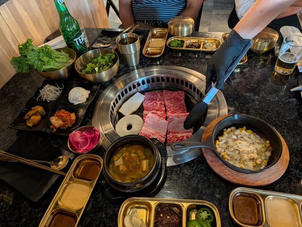 Server grilling premium Galbi short ribs at Oseyo Korean BBQ Leesburg with banchan side dishes, corn cheese, and Terra beer