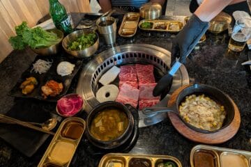 Server grilling premium Galbi short ribs at Oseyo Korean BBQ Leesburg with banchan side dishes, corn cheese, and Terra beer